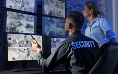 Two security personnel, one male and one female, monitor surveillance footage on multiple screens in a control room. The man is seated, holding a walkie-talkie, while the woman stands behind him, focused on the screens. Both wear uniforms labeled "SECURITY," ensuring event security in Harris County.